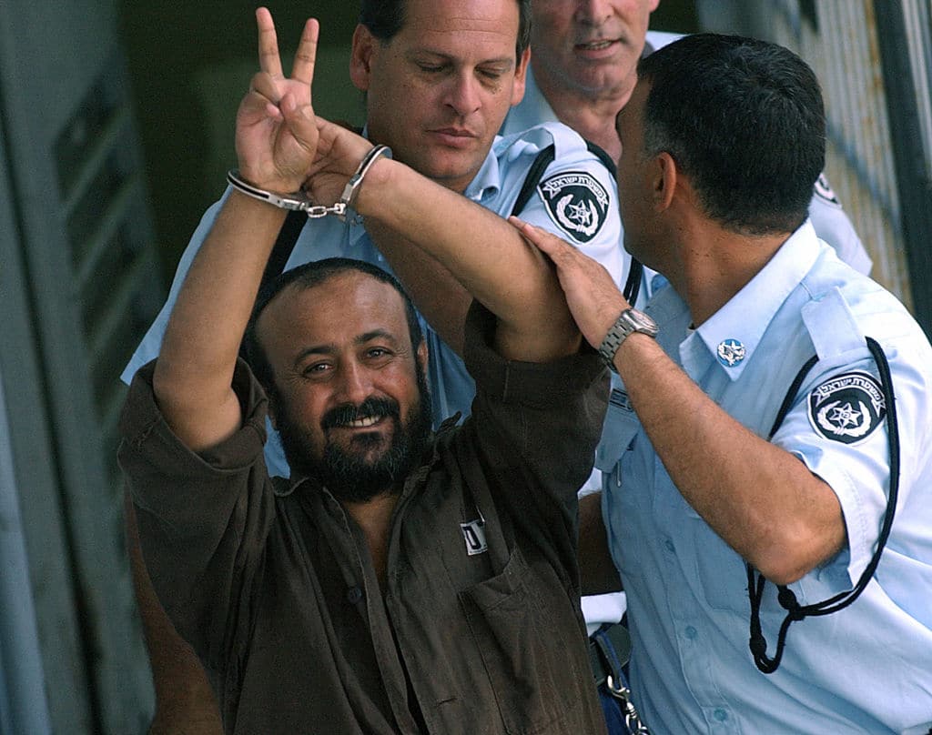 Hand cuffed and flashing the 'V'-sign, Marwan Barghuti the leader of Yasser Arafat's Fatah movement in the West Bank is flanked by Israeli policemen as he is led to a police vehicle 29 September 2003 on his way back to jail, after appearing before a Tel Aviv court.