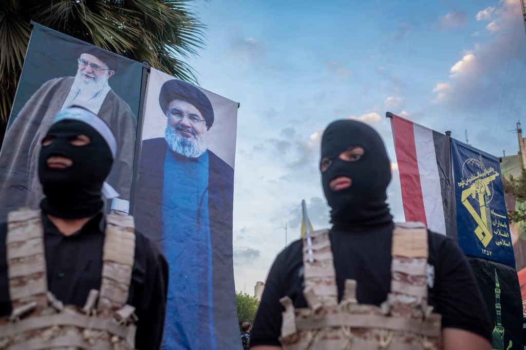 Two Islamic Revolutionary Guard Corps (IRGC) personnel, wearing masks and flak jackets, symbolize Hamas warriors and stand under the portraits of Iran's Supreme Leader, Ayatollah Ali Khamenei, Lebanon's Hezbollah late leader, Hassan Nasrallah, who is killed in an Israeli airstrike, and a flag of the IRGC during a ceremony commemorating the killed Hamas leader, Yahya Sinwar, at the Palestine Square in downtown Tehran, Iran, on October 24, 2024. (Photo by Morteza Nikoubazl/NurPhoto via Getty Images)