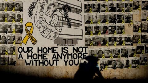 A shadow of a man seen on a wall covered with photos of hostages held in the Gaza Strip as he rides a bicycle on August 15, 2024 in Tel Aviv, Israel.