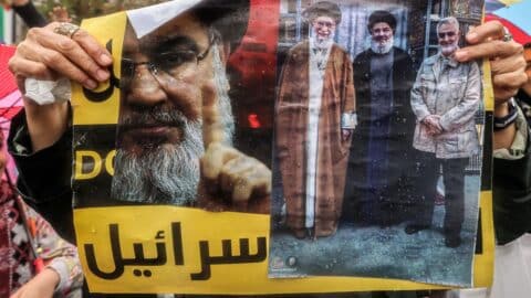 A demonstrator stands in the rain holding a picture depicting (L to R) Iran's Supreme Leader Ali Khamenei; late Lebanese Hezbollah leader Hassan Nasrallah who was killed by an Israeli air strike on September 27, 2024; and Iran's Islamic Revolutionary Guard Corps' (IRGC) Quds Force commander Qasem Soleimani who was killed by a US drone strike in January 2020; during an anti-Israel protest in Tehran's Palestine Square on September 28, 2024.