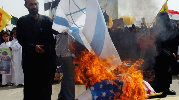 An Iraqi man burns Israeli and American flags as Iraqi women take part in a protest against Israel's attacks on civilians in Lebanon on July 31, 2006 in the Sadr Shiite city in Baghdad, Iraq. (Photo by Wathiq Khuzaie/Getty Images)