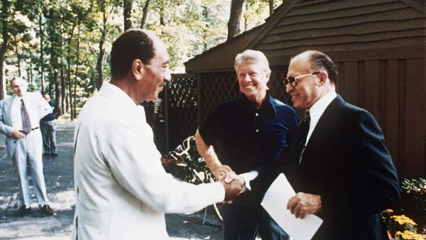 former Egyptian President Anwar al-Sadat (L) as he shakes hands with former Israeli Premier Menachem Begin, as former US President Jimmy Carter looks on, 06 September 1978 at Camp David, the US presidential retreat in Maryland. Egypt began peace initiatives with Israel in late 1977, when Sadat visited Jerusalem. A year later, with the help of Carter, terms of peace between Egypt and Israel were negotiated at Camp David. A formal treaty, signed 26 March 1979 in Washington, DC, granted full recognition of Israel by Egypt, opened trade relations between the two countries, and limited Egyptian military buildup in the Sinai. Israel agreed to return a final portion of occupied Sinai to Egypt. (Photo by various sources / AFP) (Photo by -/CONSOLIDATED NEWS/AFP via Getty Images)